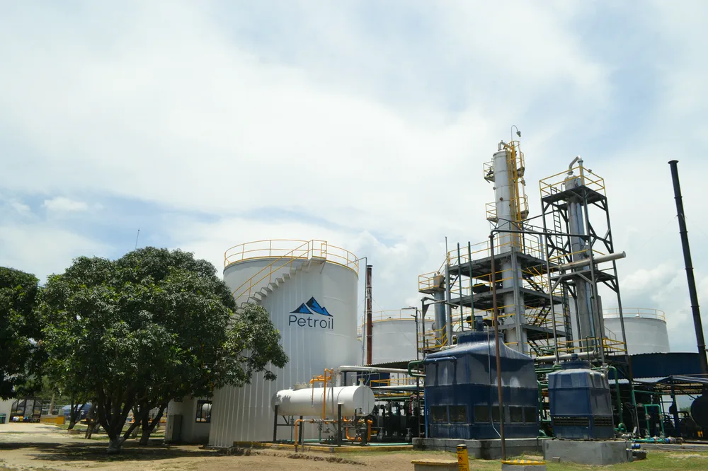 Columna de proceso y tanque de almacenamiento de la refinería, entre árboles.